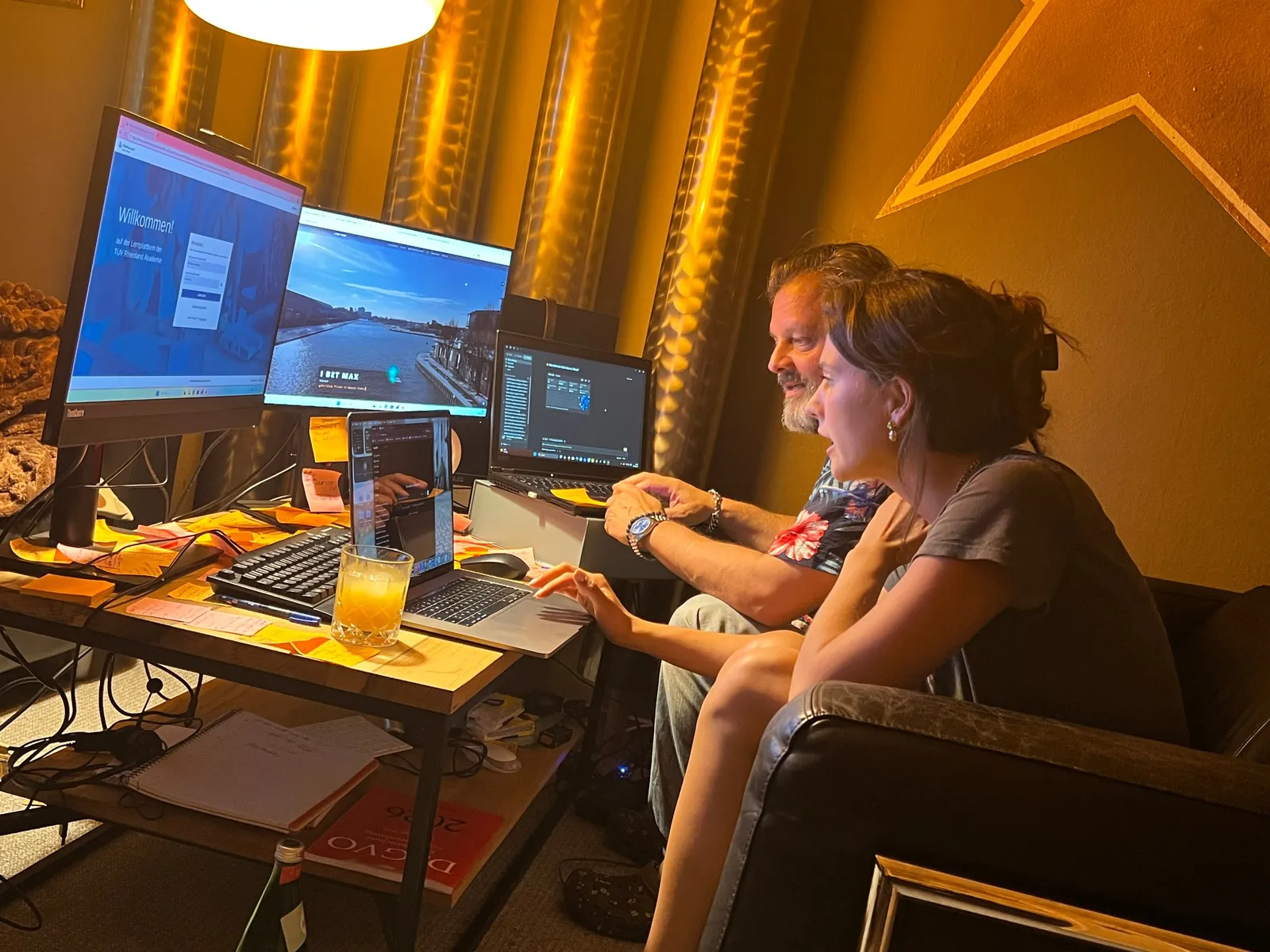 Beratungsgespräch an einem Arbeitsplatz mit mehreren Bildschirmen: Ein Berater und eine Teilnehmerin schauen gemeinsam auf die Monitore, sie bedient den Laptop.
