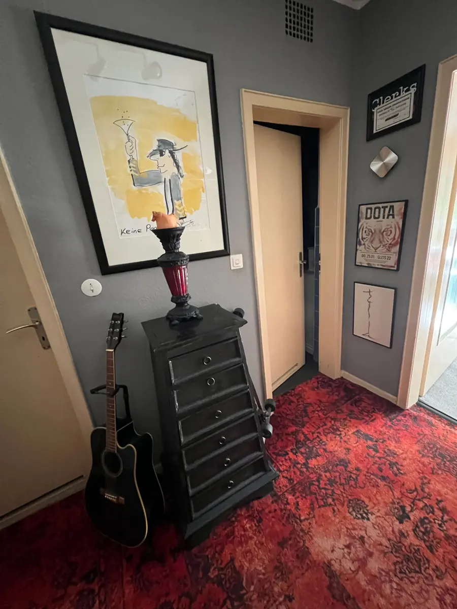 Flur mit gerahmtem Bild, schwarzer Kommode, Gitarre und rotem Teppich